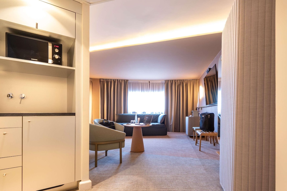 A hotel room with a sofa, armchair, coffee table, and a TV.