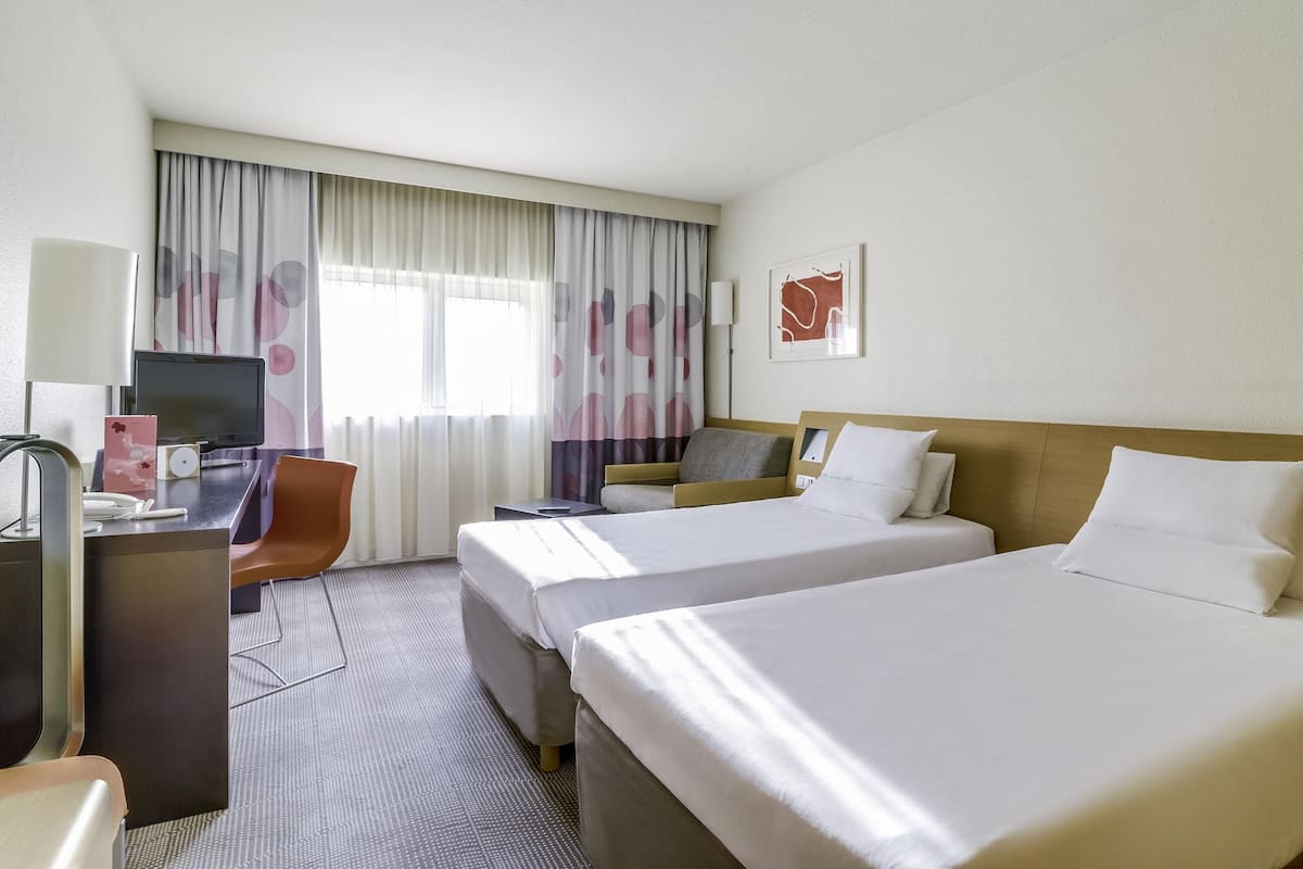 A hotel room with two beds, a desk with a computer, a chair, and a TV.
