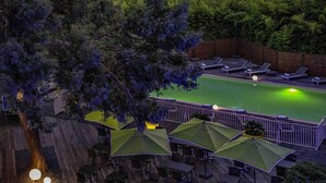 A deck with tables and chairs, a pool, and umbrellas.