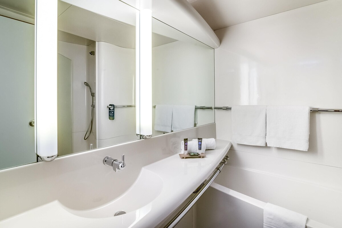 A modern bathroom with a large mirror, a white sink, a shower, and a towel rack.