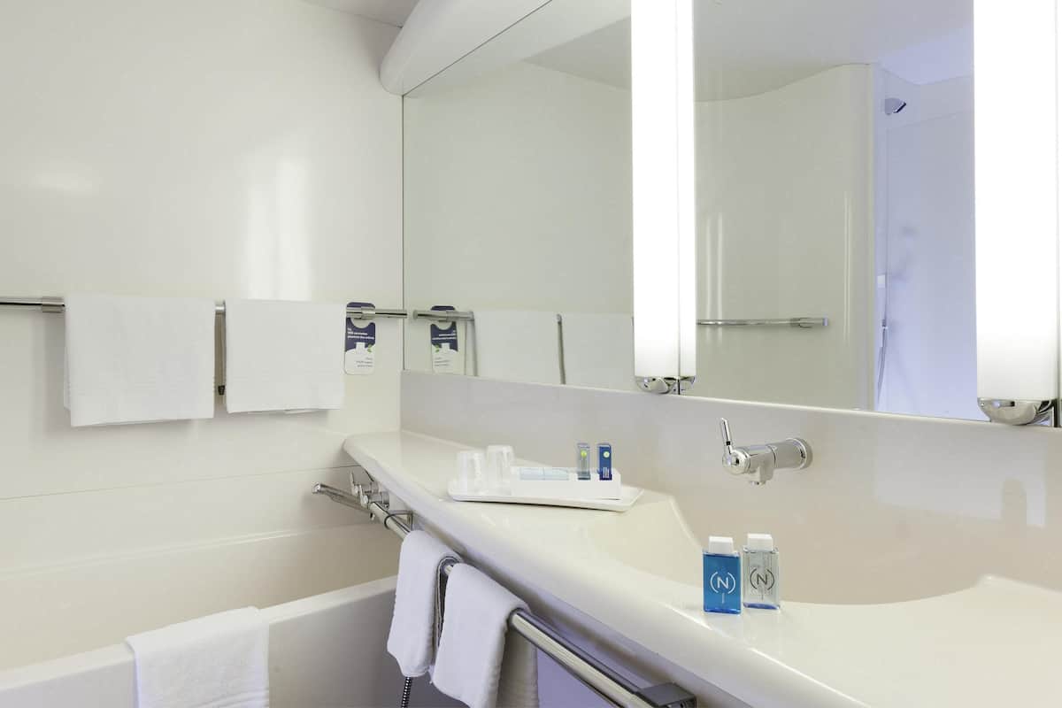 A modern bathroom with a bathtub, a large mirror, and a countertop with toiletries.