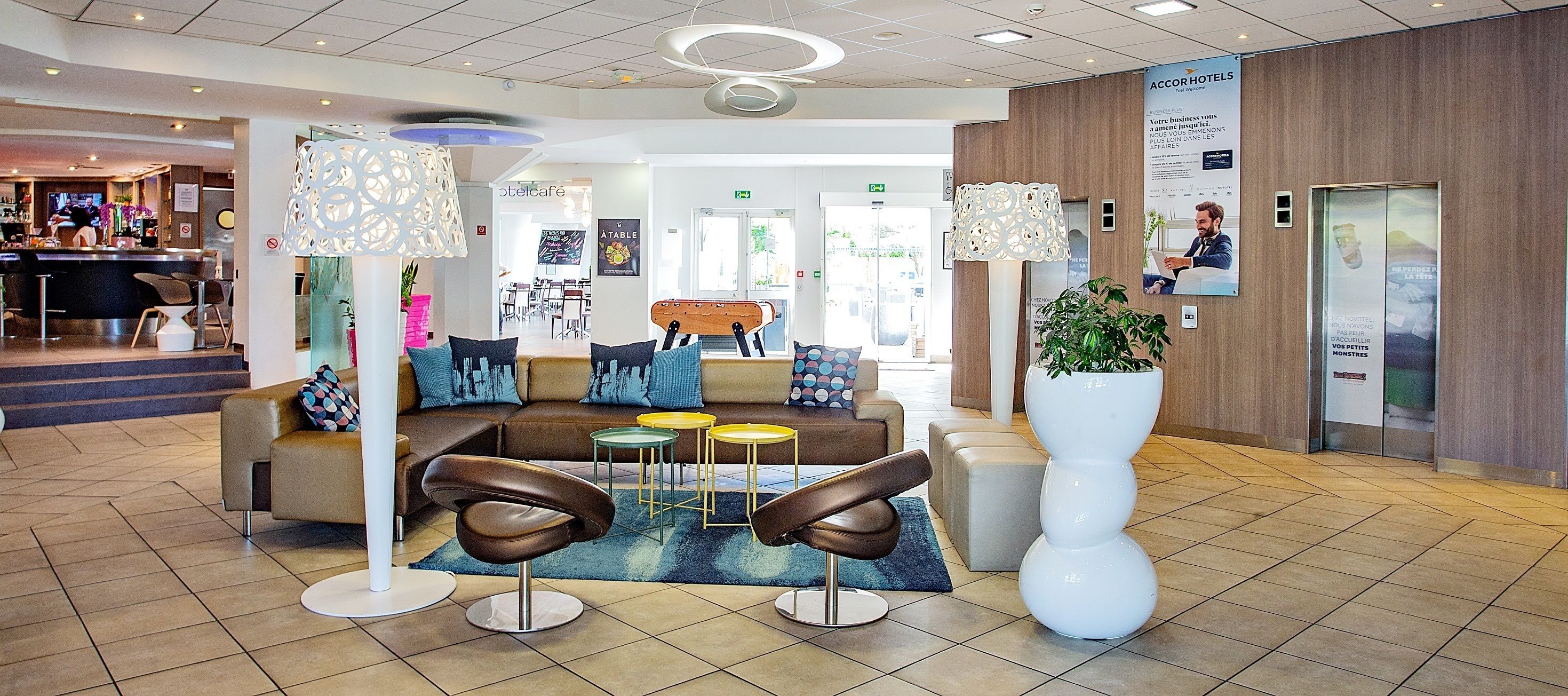 A modern lobby with a reception desk, seating area, and a large potted plant.