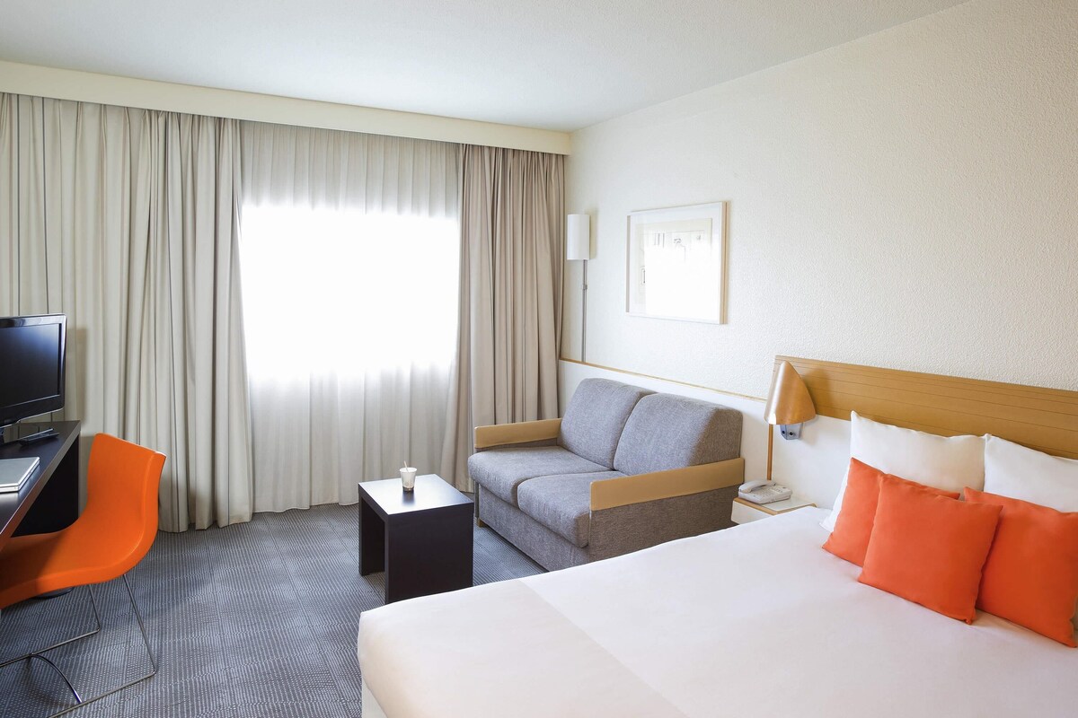 A hotel room with a bed, a sofa, a desk with a computer, and a chair.
