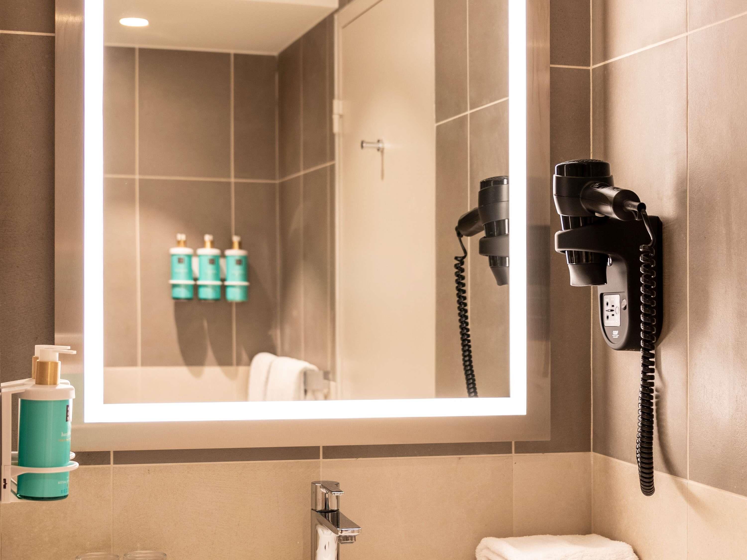A bathroom with a mirror, a hairdryer, and toiletries.