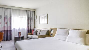 A hotel room with a large bed, a chair, a bedside table, and a window with curtains.