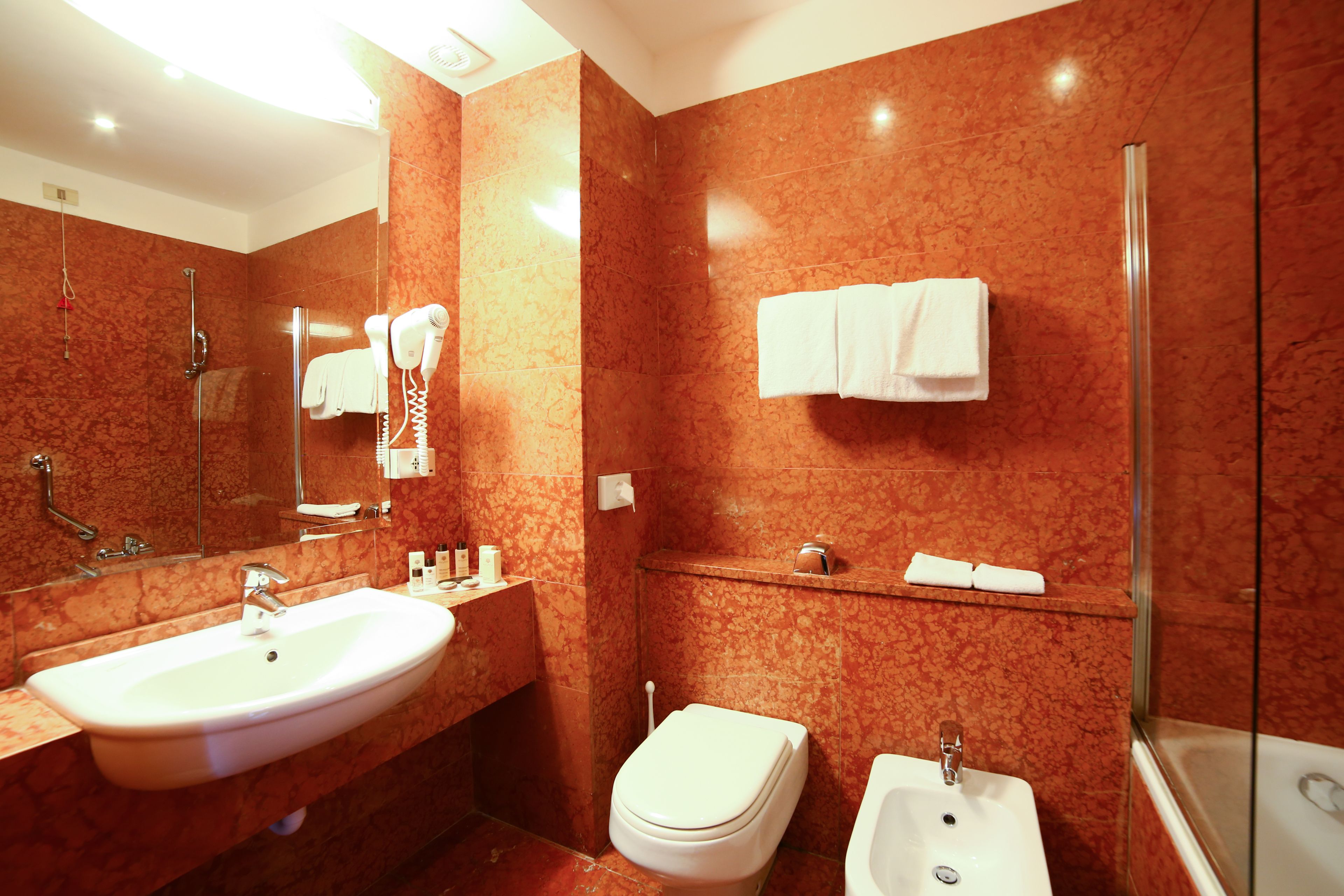 Une salle de bain moderne avec un lavabo en marbre, des toilettes, un bidet et une douche à parois de verre.