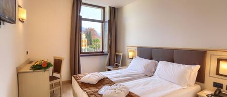 A hotel room with a bed, a desk, a chair, and a window with curtains.