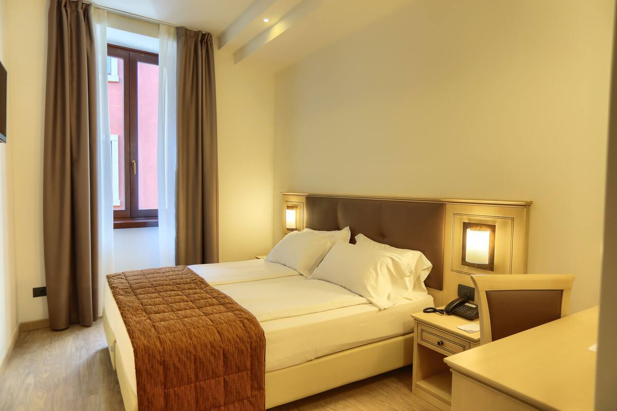 Ein Hotelzimmer mit einem Bett, einem Nachttisch mit Telefon und einem Fenster mit Vorhängen.