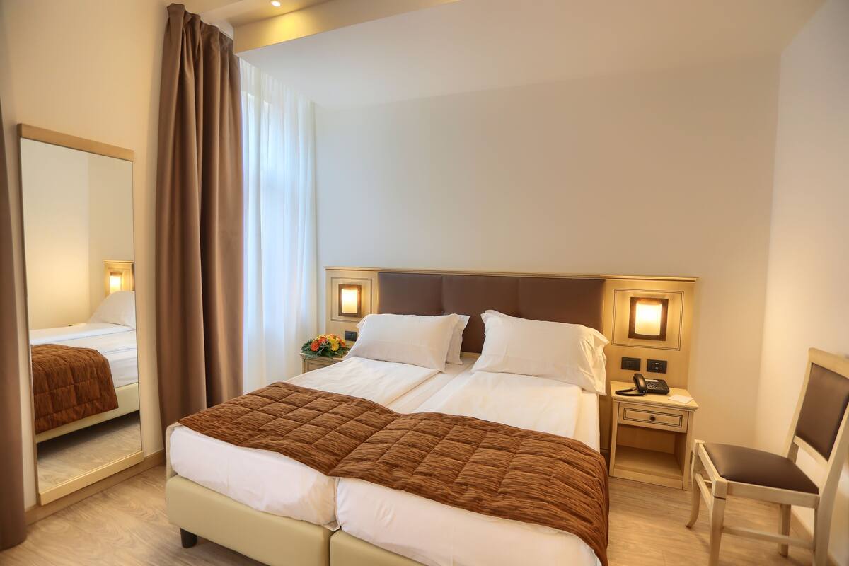 Ein Hotelzimmer mit einem großen Bett, einem Nachttisch mit Lampe, einem Sessel und einem Spiegel.