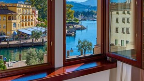 Ein Hotelzimmer mit einem großen Bogenfenster mit Blick auf ein Gewässer, einen Steg und ein Gebirge.