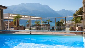 Ein Pool mit klarem, blauem Wasser, umgeben von Liegestühlen und Palmen, mit Blick auf eine Berglandschaft im Hintergrund.