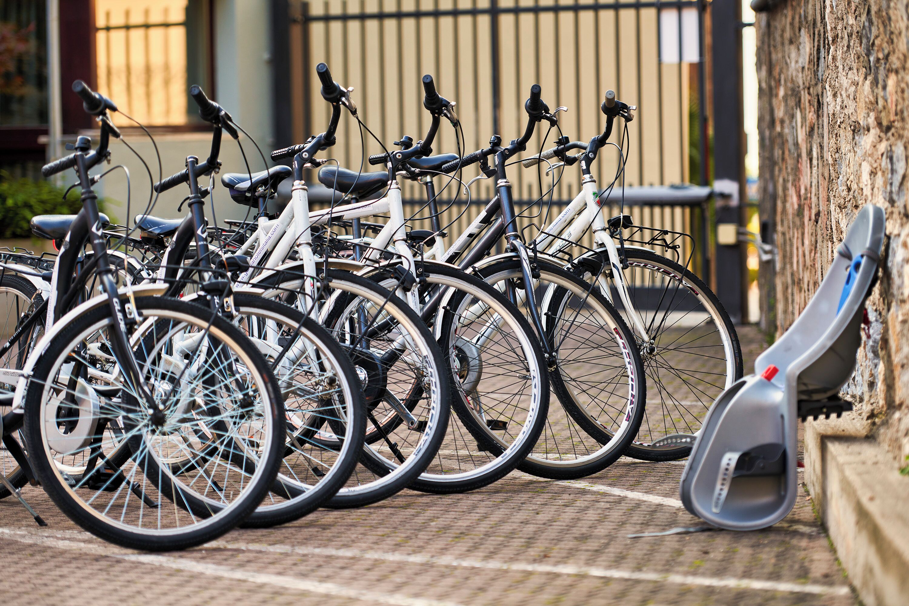 Una fila de bicicletas estacionadas en un área designada, con un muro de concreto y una reja metálica al fondo.