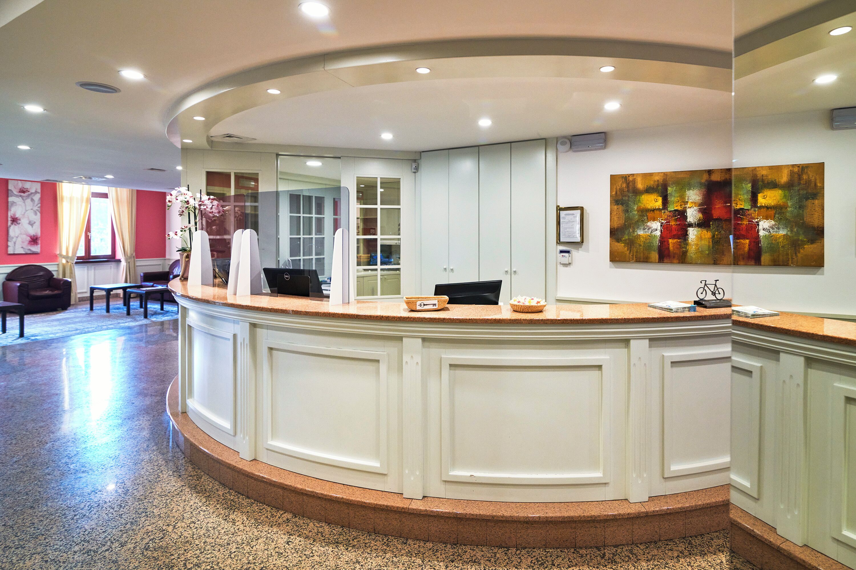 A reception area with a curved counter, a seating area with a sofa and chairs, and a large abstract painting on the wall.