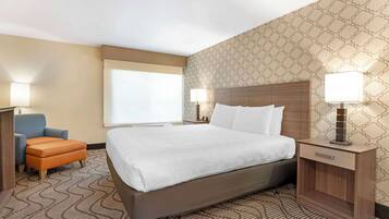 A hotel room with a large bed, a nightstand with a lamp, a blue armchair, and a patterned carpet.
