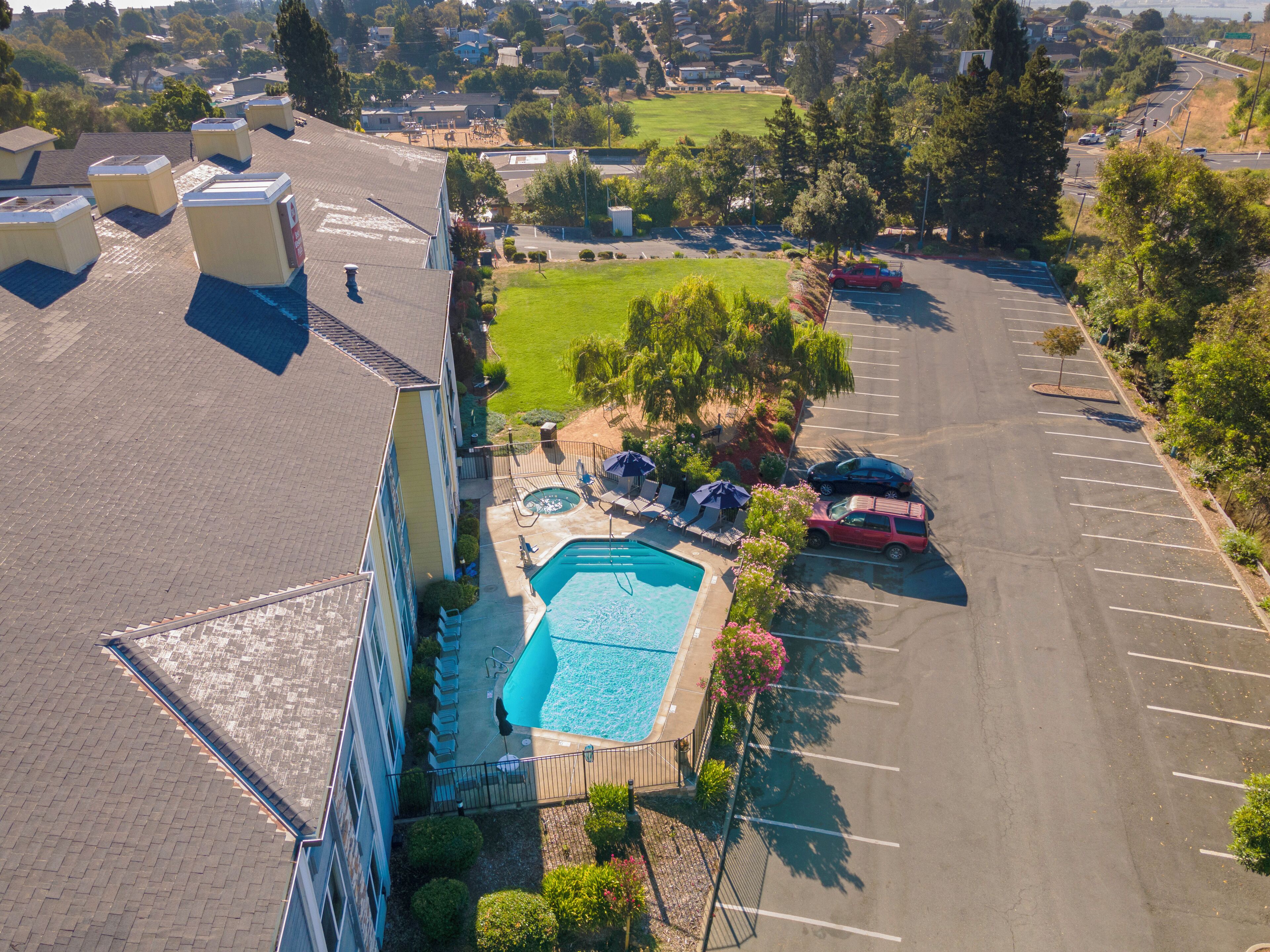 An aerial view of a residential area with a swimming pool, a parking lot, and a building with multiple air conditioning units on the roof.