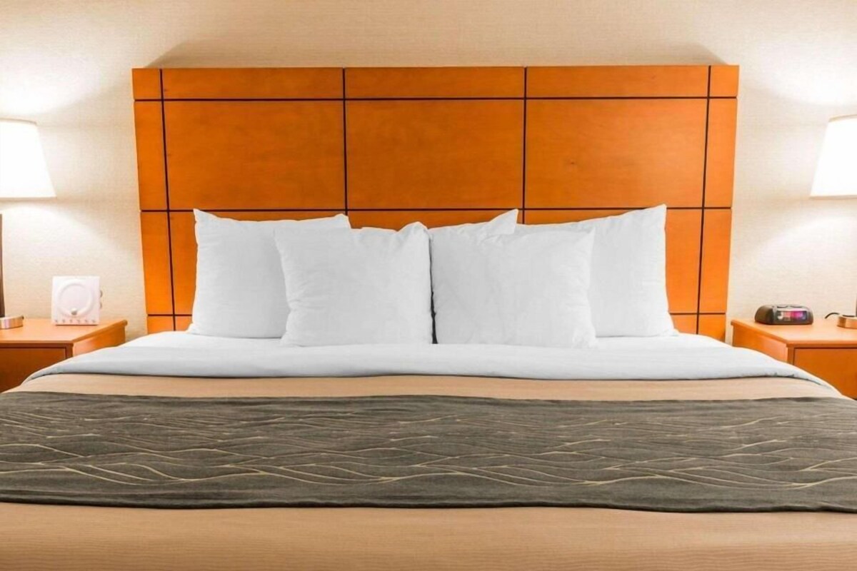 A hotel room with a large bed, a wooden headboard, two bedside tables, and a nightstand.