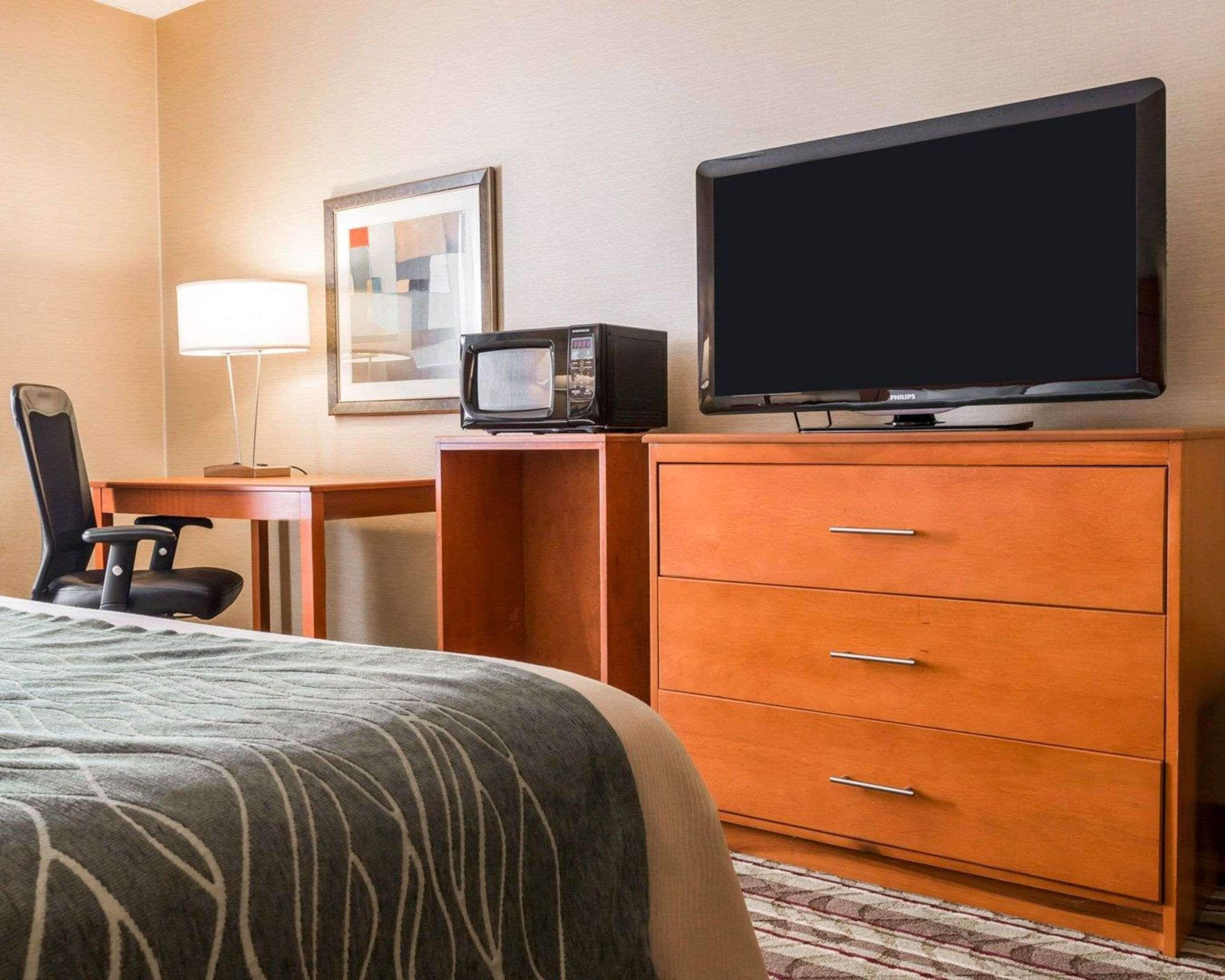 Ein Hotelzimmer mit Bett, Schreibtisch mit Lampe, Fernseher, Mikrowelle und Kommode.