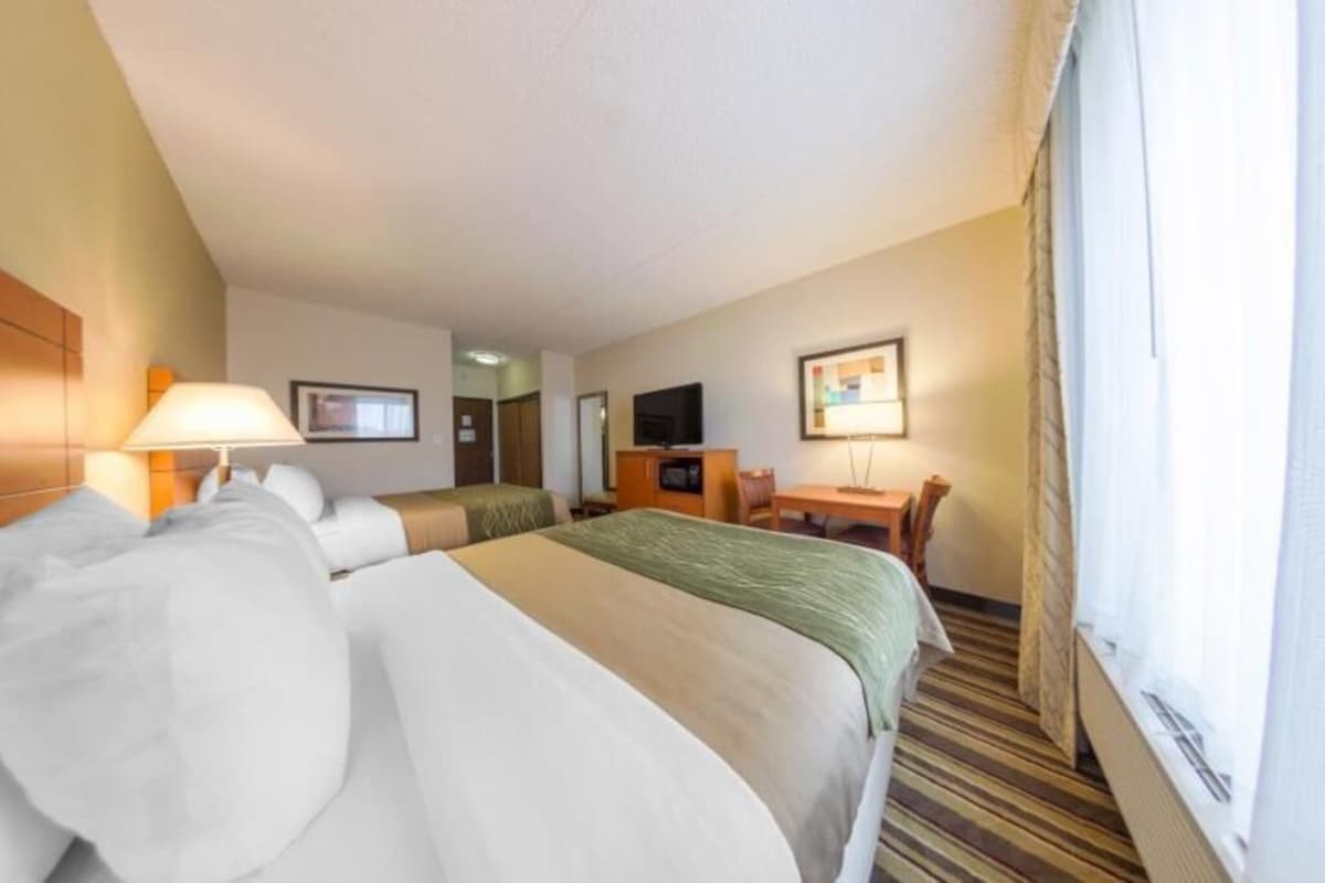 A hotel room with two beds, a desk, a chair, a television, and a window with curtains.