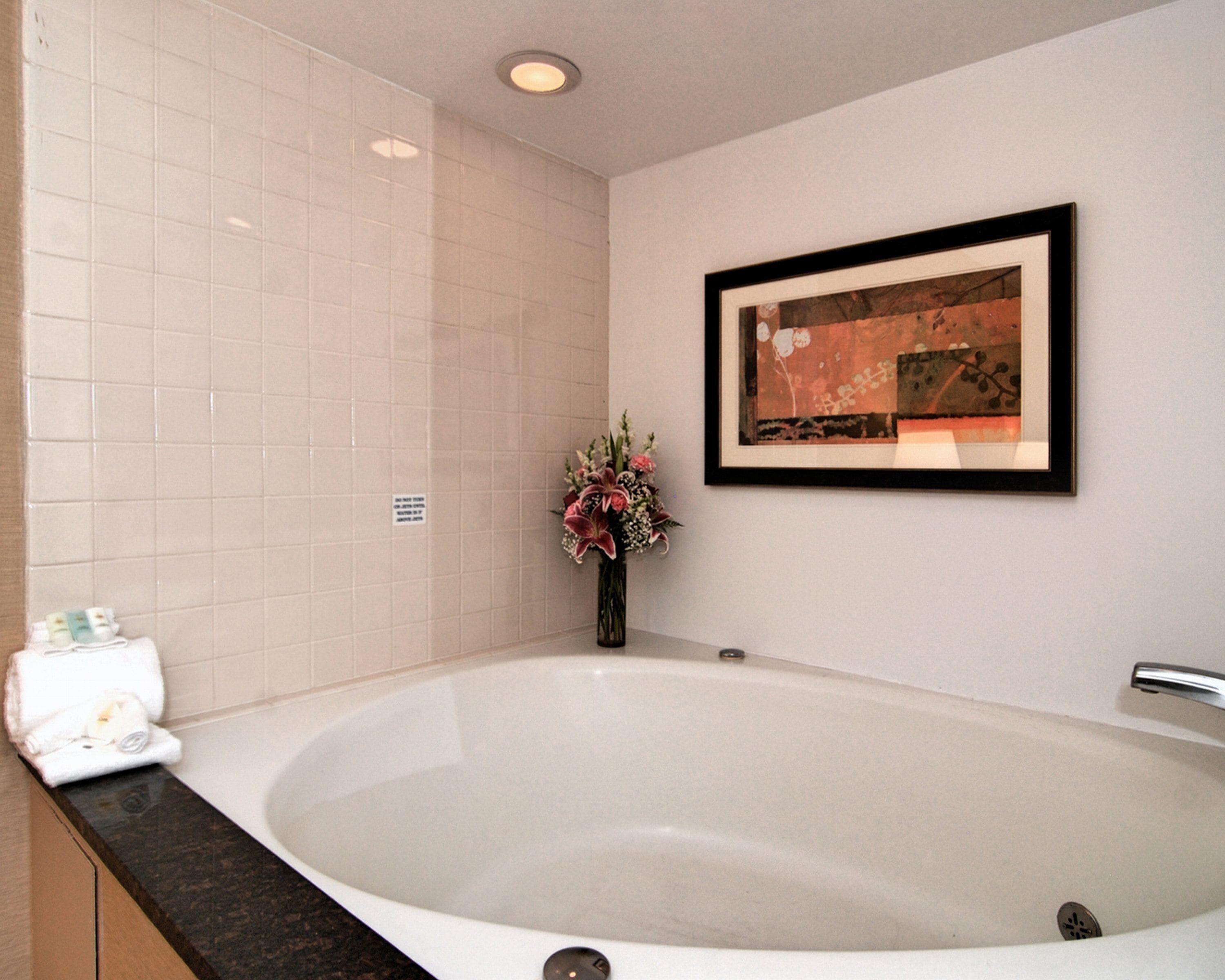 A bathroom with a large bathtub, a framed artwork on the wall, and a vase with flowers on the counter.