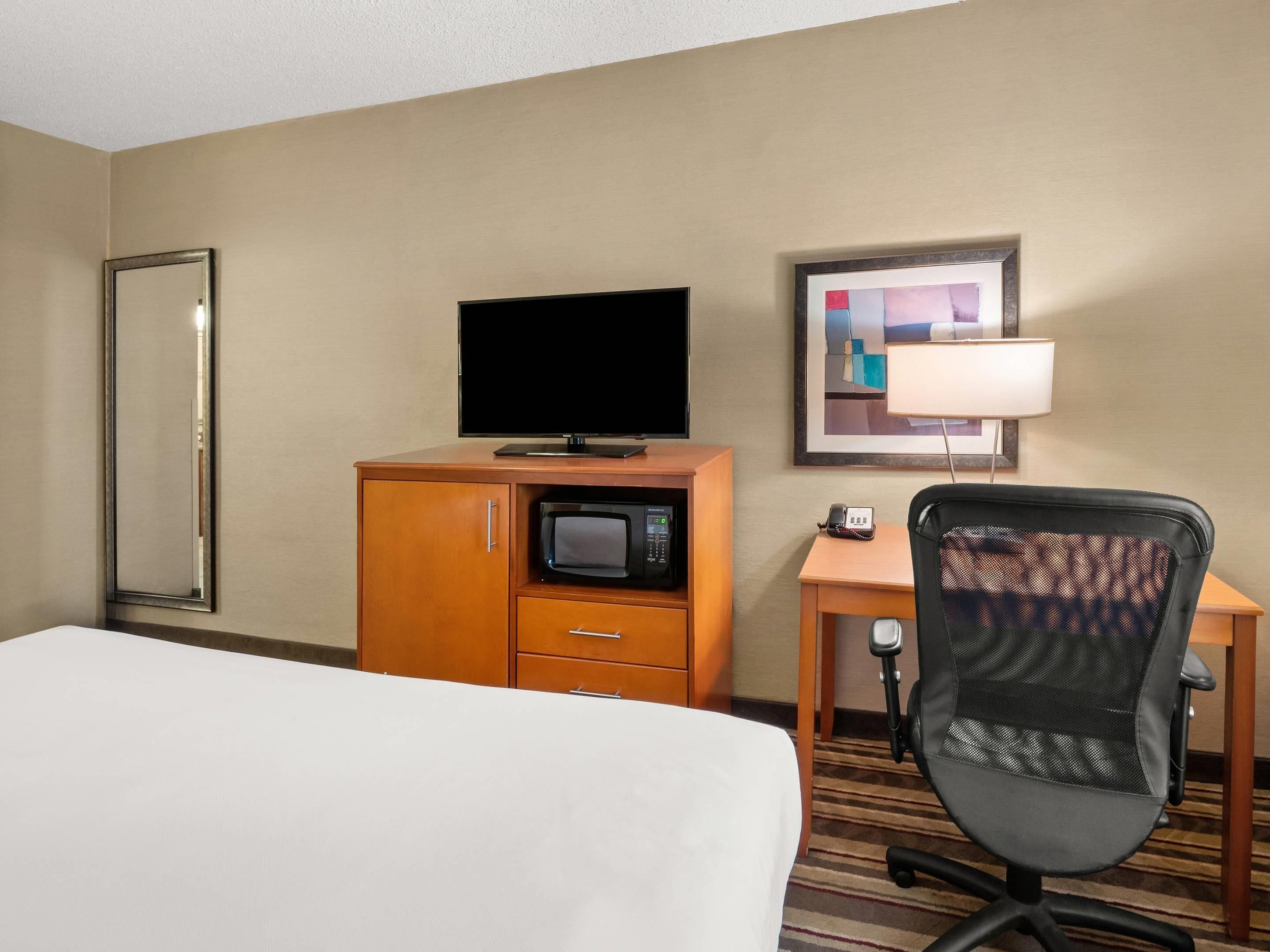 A hotel room with a bed, a wooden desk with a telephone, a television, a microwave, and a chair.