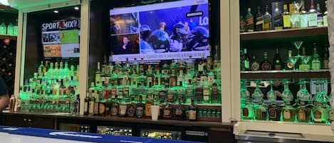 A bar area with a large screen displaying sports content, shelves of various liquor bottles, and a sign for 'SPORT MIX'.