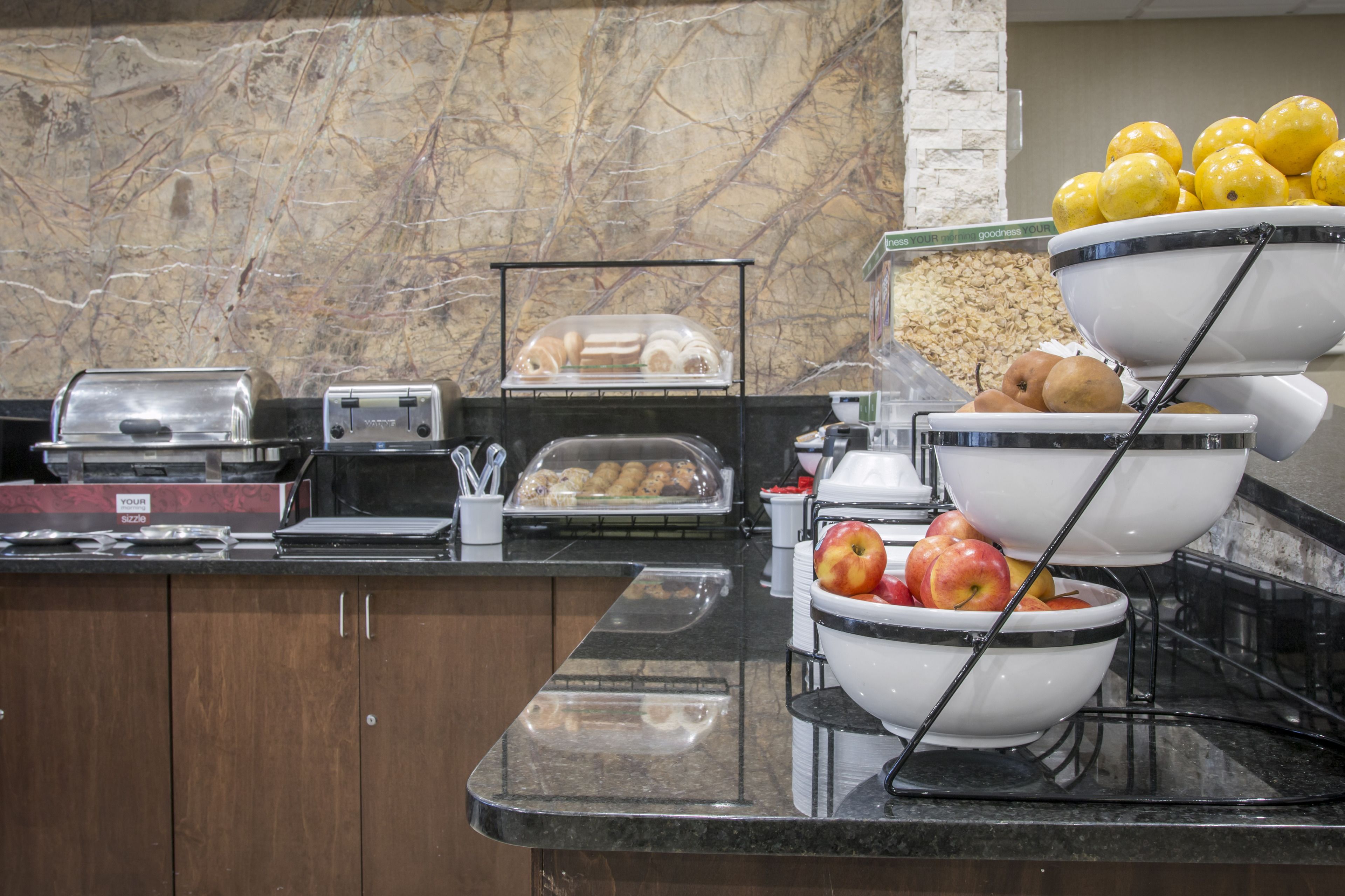 A buffet setup with a variety of food items, including fruits and pastries, on a marble countertop.