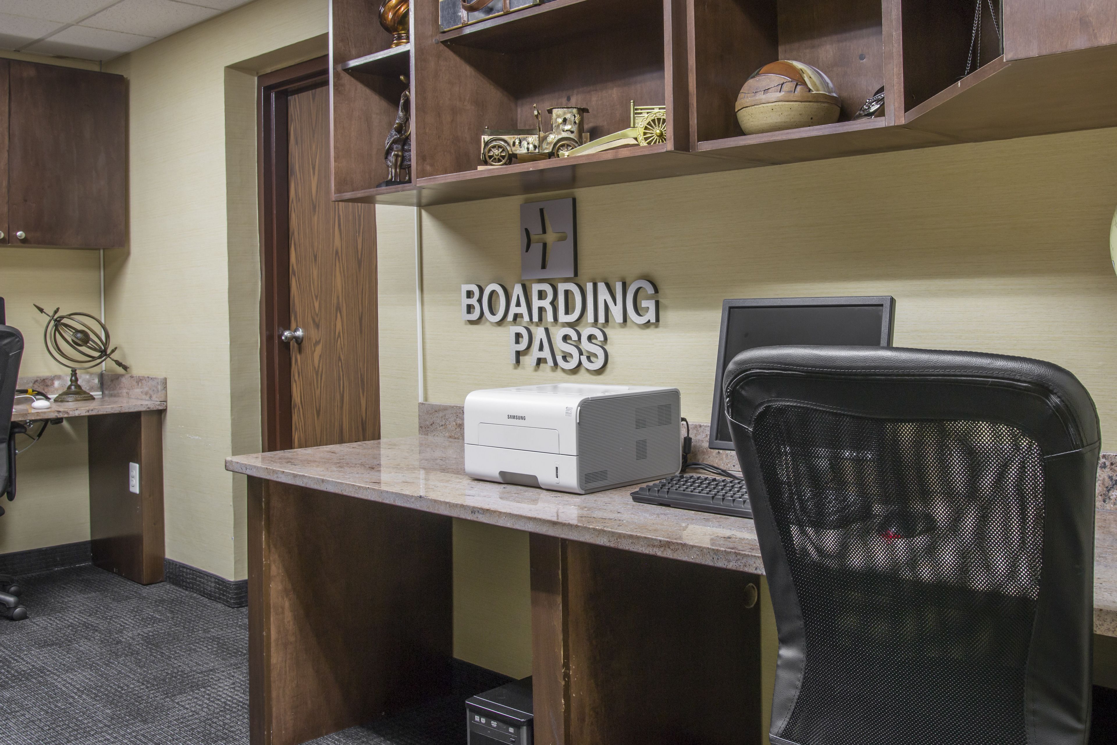 A desk with a Samsung printer, a computer, and a chair. There is a 'Boarding Pass' sign on the wall.
