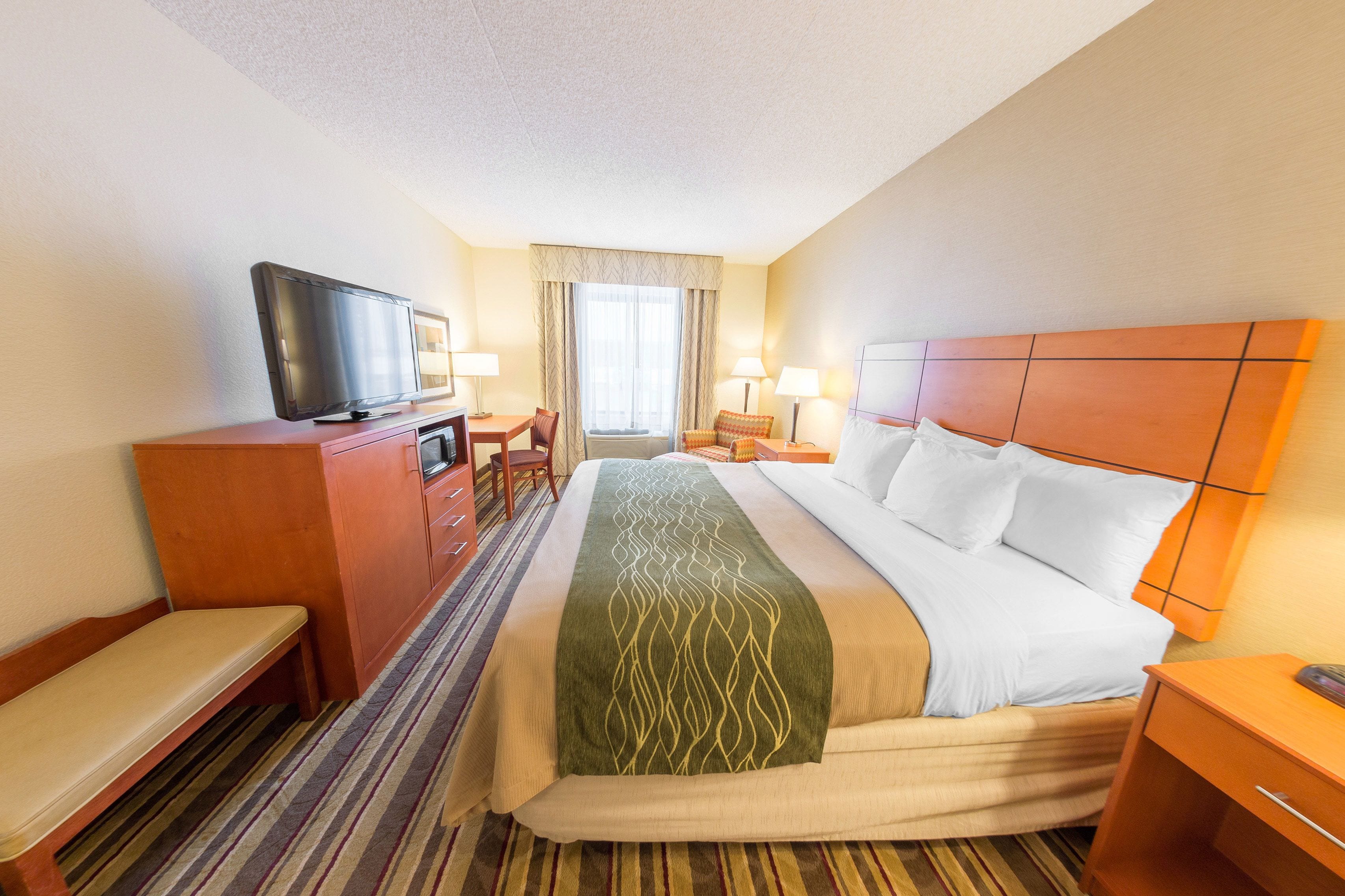 A hotel room with a bed, a television on a wooden cabinet, a desk with a chair, and a window with curtains.