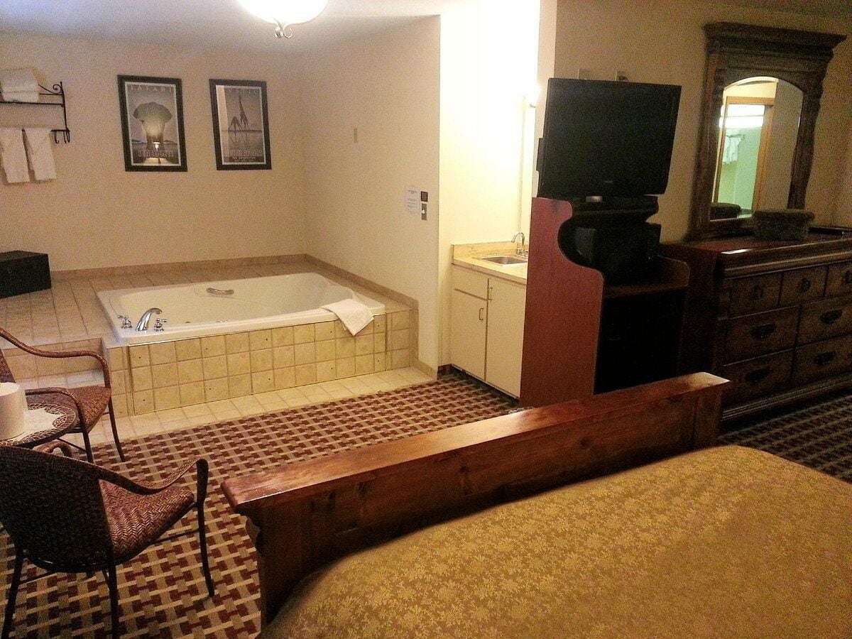 Habitación de hotel con bañera, televisor, banco de madera y una silla.