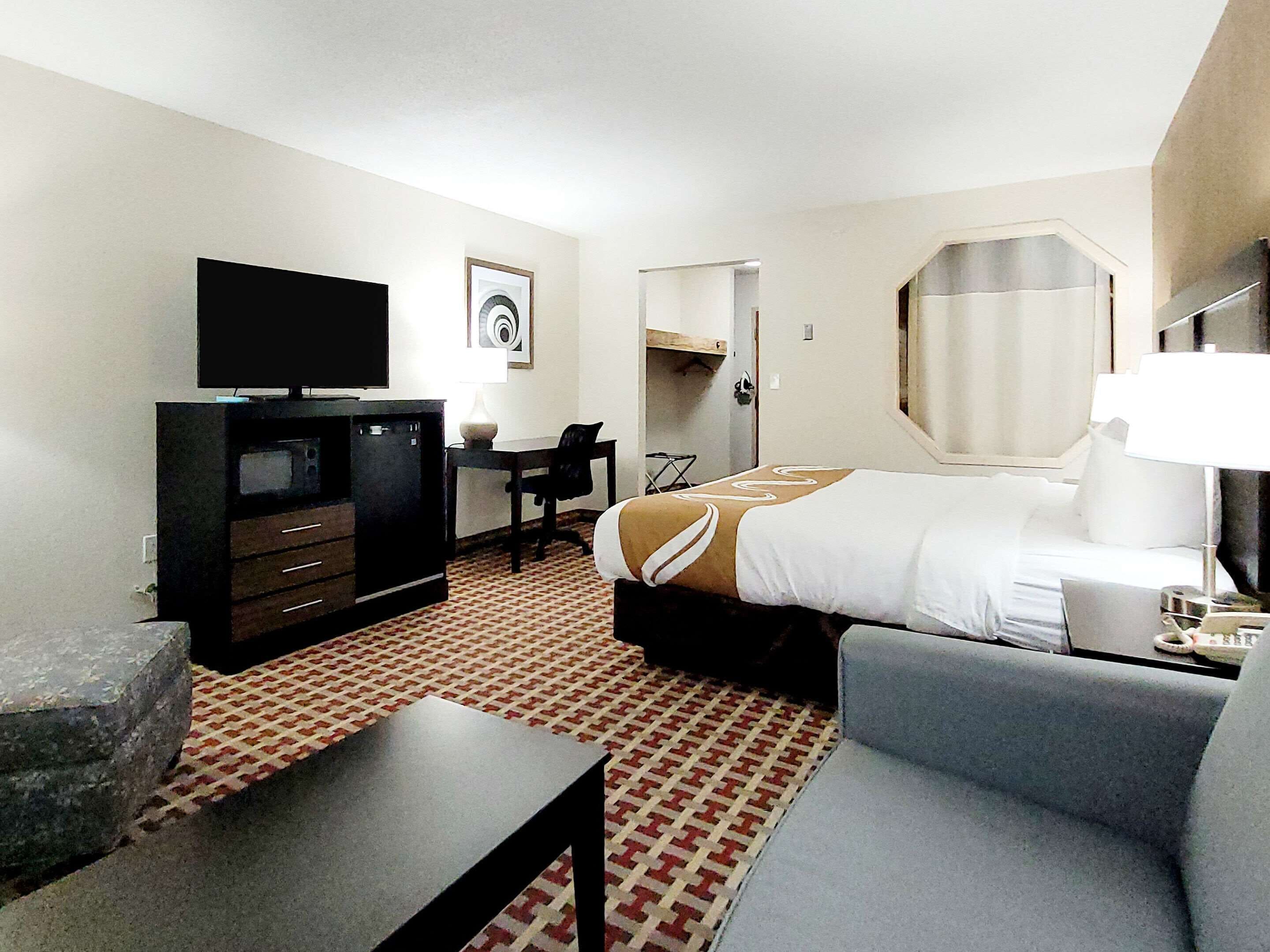A hotel room with a bed, a desk, a television, a chair, and a small table.