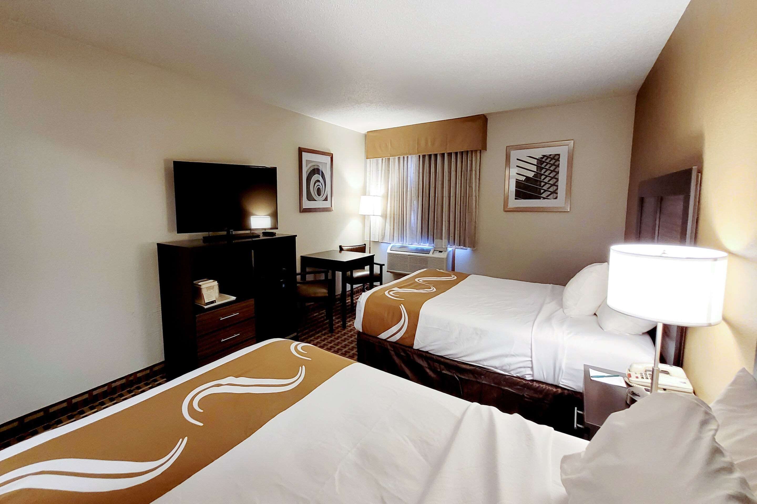 A hotel room with two beds, a desk, a television, and a window with curtains.
