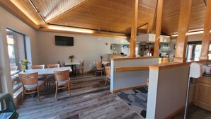 A dining area with wooden tables and chairs, a TV mounted on the wall, and a kitchen area with wooden cabinets and a countertop. - Quality Inn & Suites Marion (Marion)