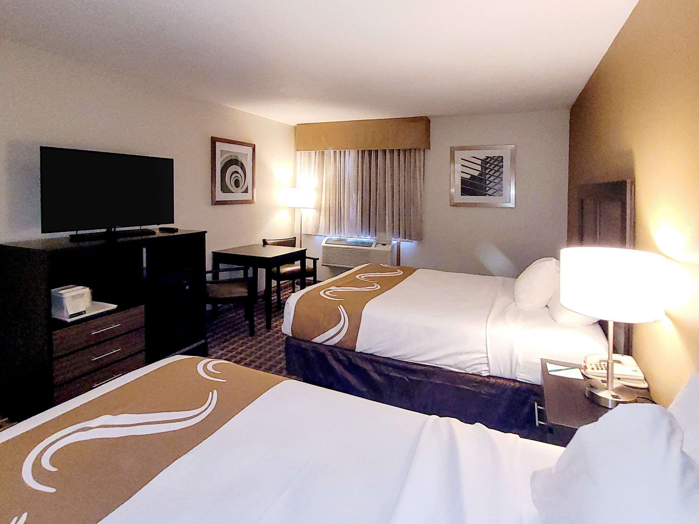 A hotel room with two beds, a desk, a TV, and a lamp.