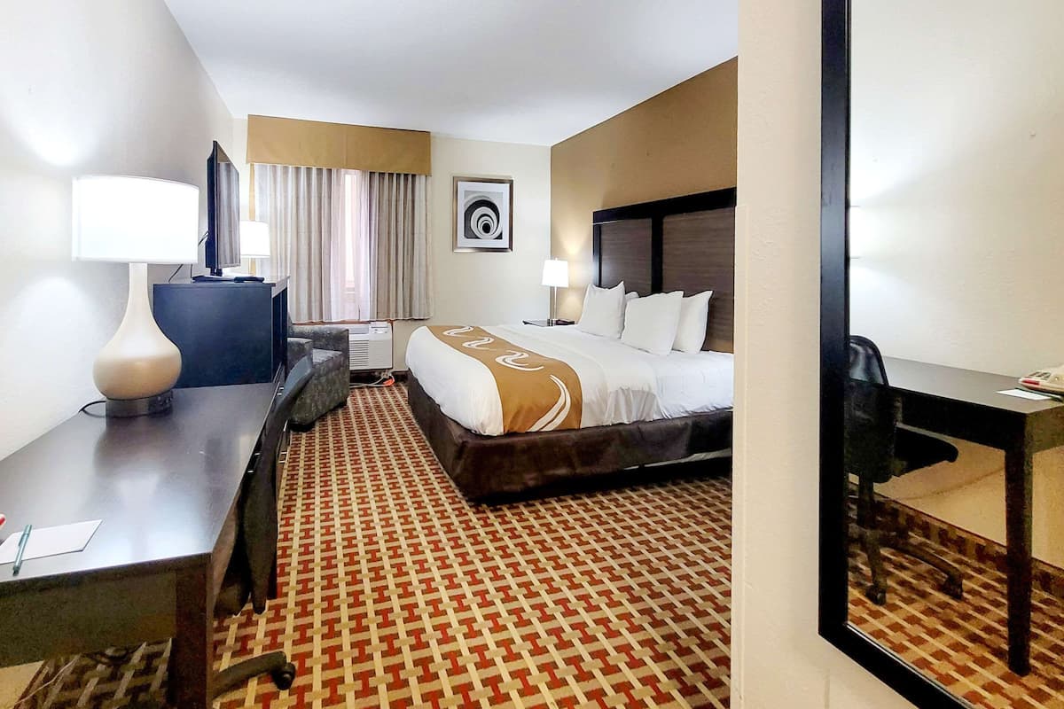 Quarto de hotel com cama, escrivaninha, cadeira e um espelho grande.