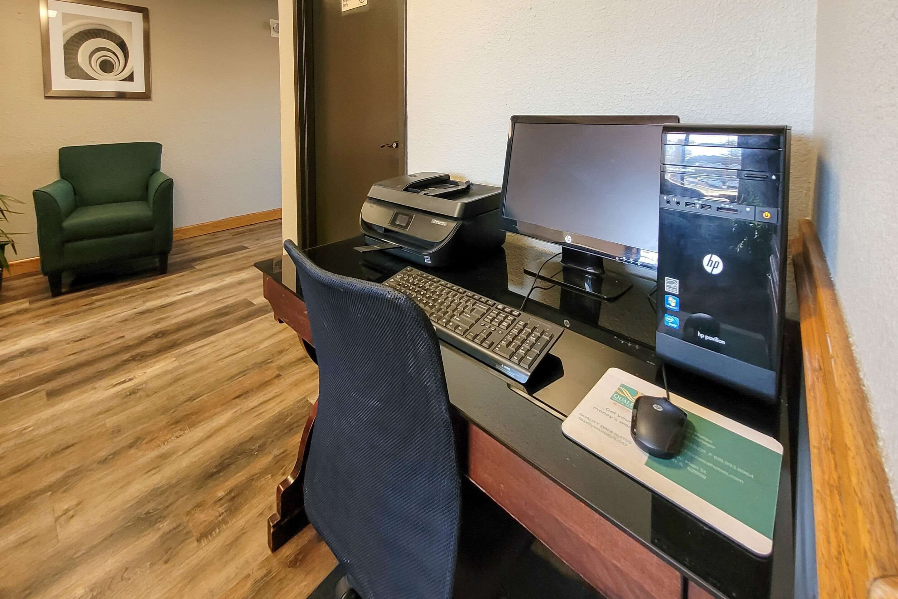 A hotel workspace with a desktop computer, printer, and a green chair.