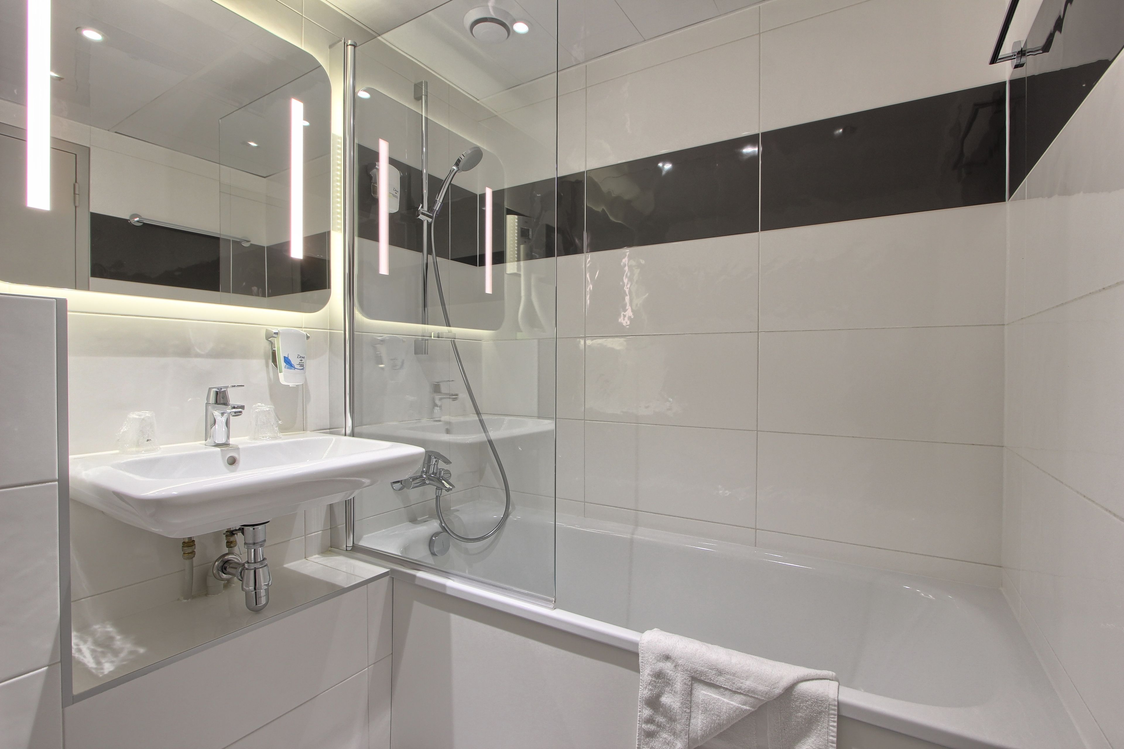 A modern bathroom with a large mirror, two sinks, a shower, and a bathtub.