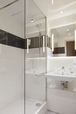 Une salle de bain moderne avec une douche à parois de verre, un lavabo blanc et un miroir au-dessus.