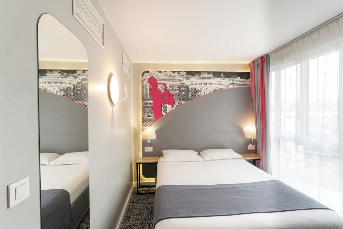 Une chambre d’hôtel avec un lit, une table de chevet, un miroir et une fenêtre avec des rideaux.