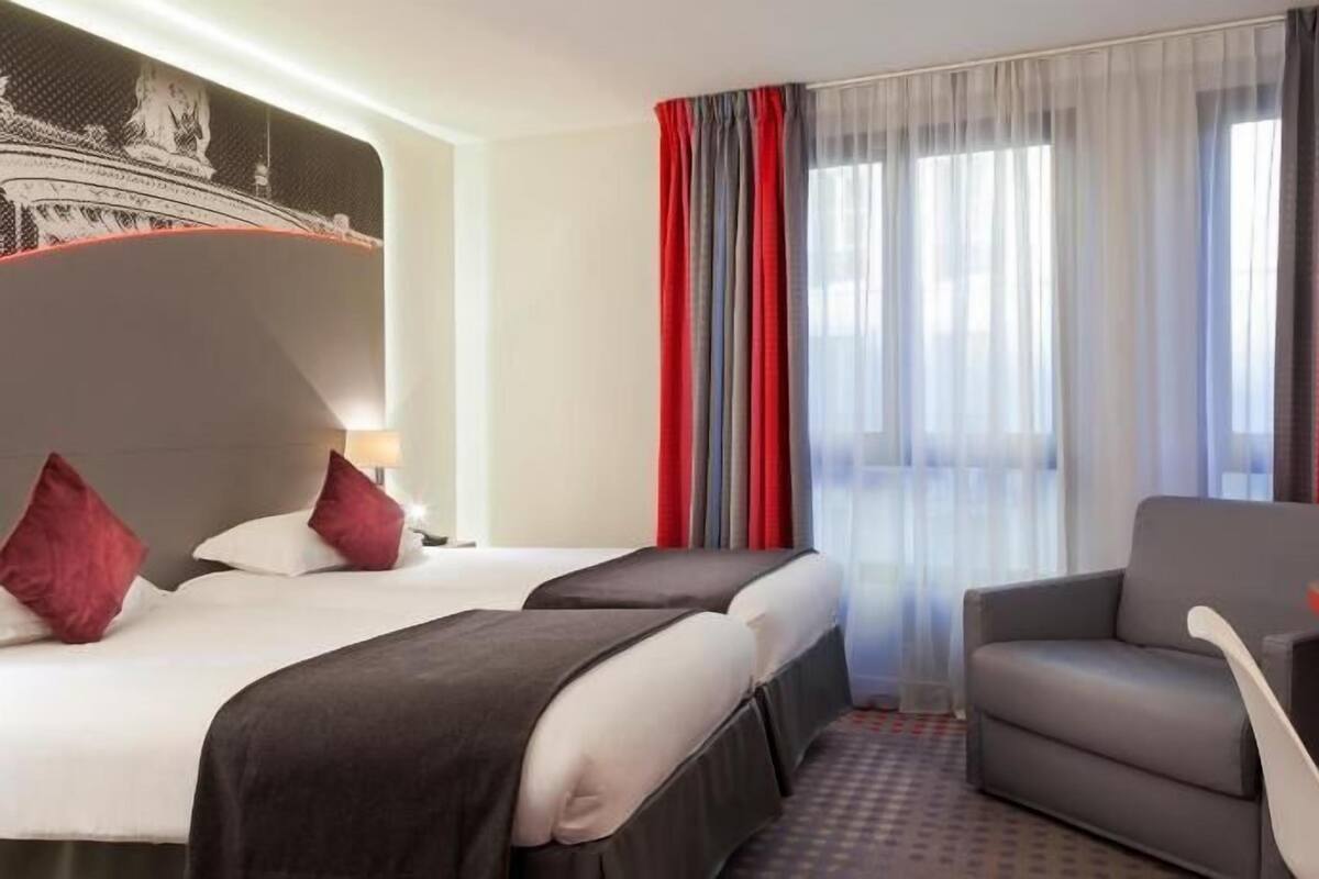 Une chambre d’hôtel avec deux lits, un bureau avec une machine à café, une télévision et une grande fenêtre avec des rideaux.