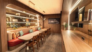 A modern dining area with a long wooden table, cushioned seating, and a built-in TV. - Hotel Inn Design Paris Place d'Italie (Paris)