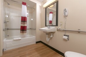 A bathroom with a bathtub, a sink, a toilet, a shower, and a hairdryer on the wall. - Red Roof Inn PLUS+ West Springfield (West Springfield)