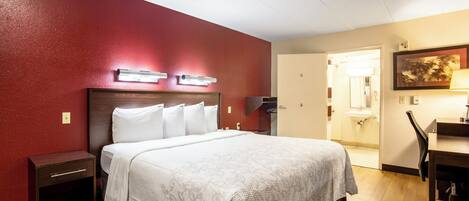 Ein Hotelzimmer mit einem Bett, Nachttischen, einem Schreibtisch und einem Sessel. Eine Tür führt ins Badezimmer.