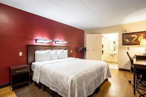 A hotel room with a bed, bedside tables, a desk, and a chair. There is a door leading to a bathroom.