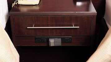 Una mesita de noche de madera con un teléfono, un cajón con asa y un enchufe con un cargador Canon.
