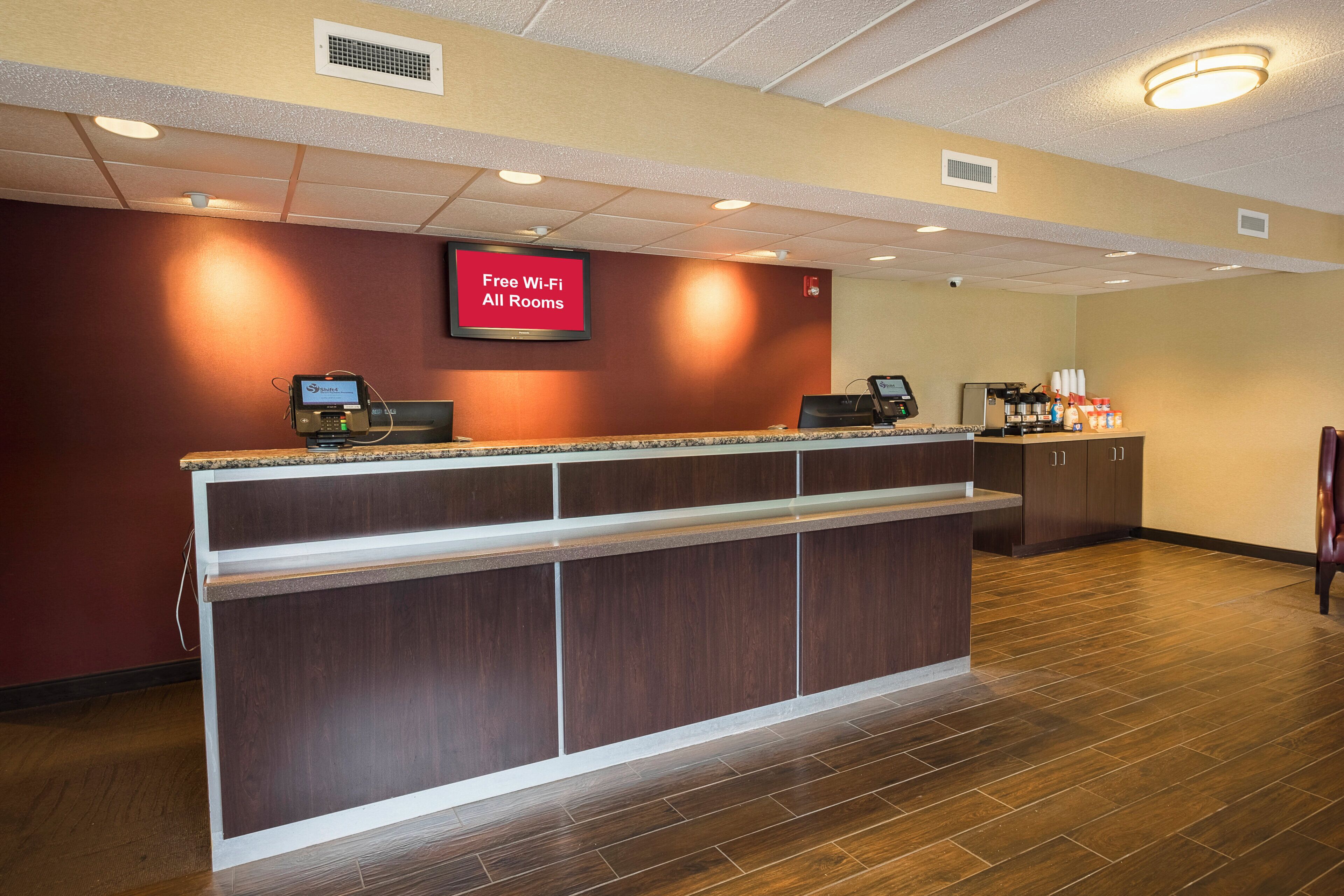 A hotel reception area with a digital screen advertising free Wi-Fi, a self-service kiosk, and a coffee station.