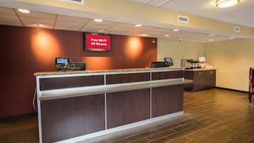 A hotel reception area with a digital screen advertising free Wi-Fi, a self-service kiosk, and a coffee station.