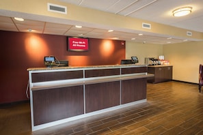A hotel reception area with a digital screen advertising free Wi-Fi, a self-service kiosk, and a coffee station.