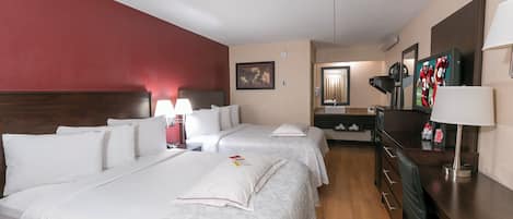 A hotel room with two beds, a desk, a mirror, and a television.