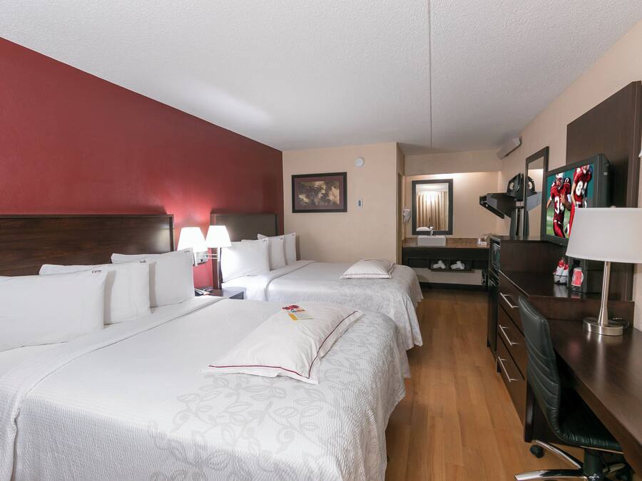 A hotel room with two beds, a desk, a mirror, and a television.