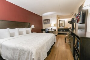 A hotel room with a large bed, a desk with a chair, a refrigerator, and a television. - Red Roof Inn PLUS+ West Springfield (West Springfield)